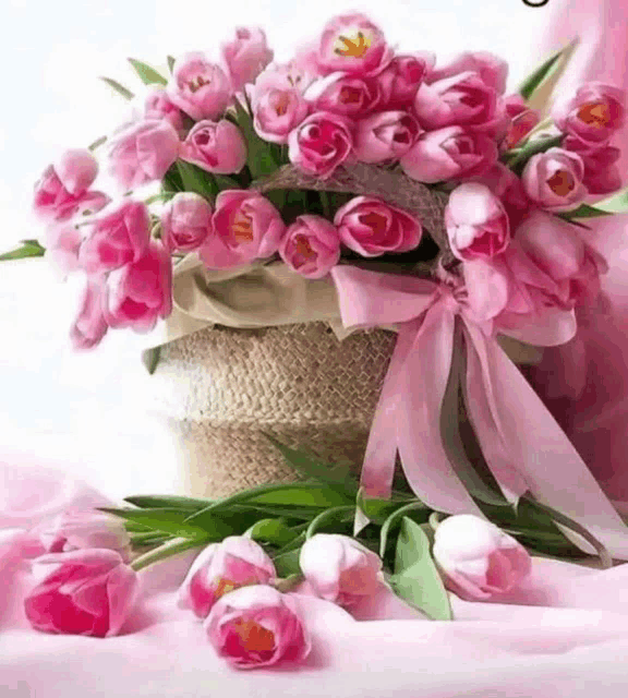 a basket filled with pink flowers with a pink ribbon on a table .