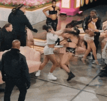 a group of women are dancing in a room with a man in a black jacket standing behind them