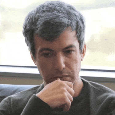 a man with gray hair is sitting in front of a window with his hand to his chin