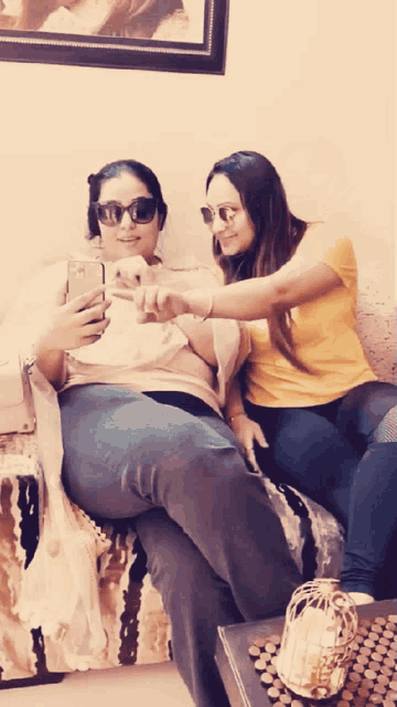 two women sitting on a couch looking at a phone