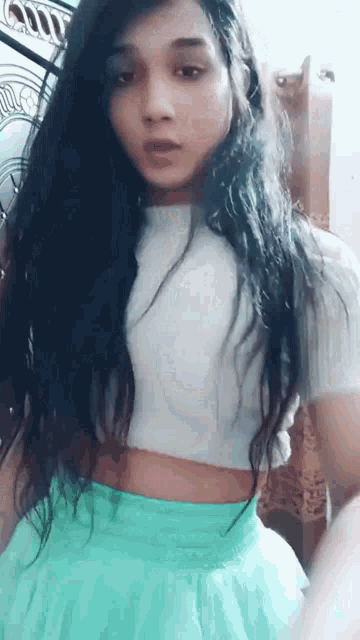 a girl with long black hair is wearing a white crop top and a green skirt .