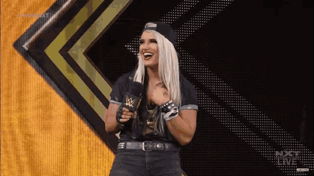 a female wrestler is holding a microphone in front of a screen that says nxt live on it
