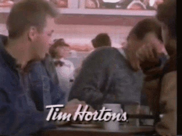 two men are sitting at a table in front of a tim hortons sign