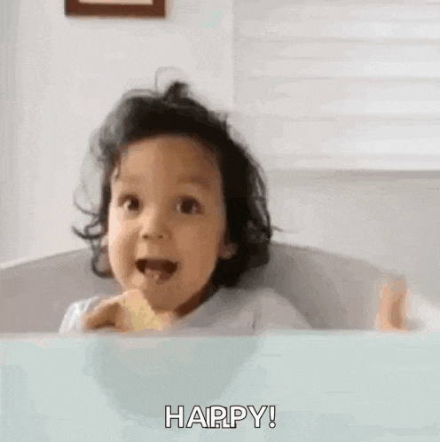a little girl is sitting at a table with her mouth open and giving a thumbs up sign .