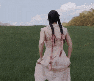 a woman in a pink dress is standing in a grassy field with her hands in her pockets .