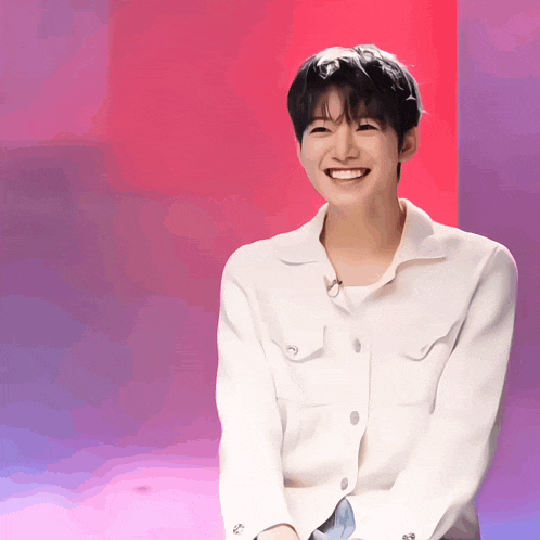 a young man wearing a white shirt is smiling in front of a pink and purple wall