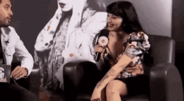 a woman is sitting in a chair holding a microphone and smiling while talking to a man .