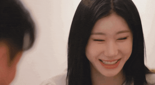 a woman with long black hair is smiling and looking at another woman .