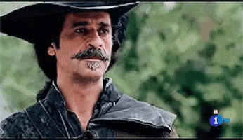 a man with a mustache is wearing a cowboy hat and a hood .