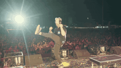 a man kicks his leg in the air while standing on a stage in front of a crowd