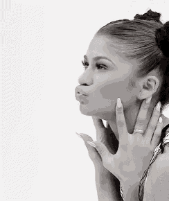 a black and white photo of a woman blowing a kiss with her hand .