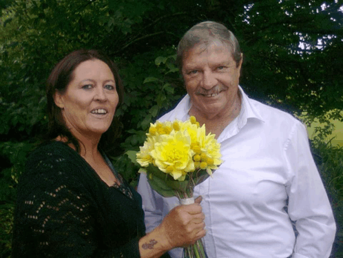 a man and a woman standing next to each other holding a bouquet of yellow flowers