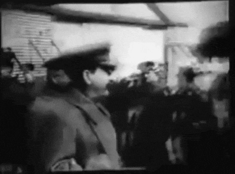 a black and white photo of a man in a military uniform saluting a crowd of people .