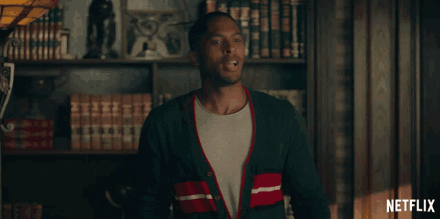 a man in a green cardigan is standing in front of a bookshelf with netflix written on the bottom