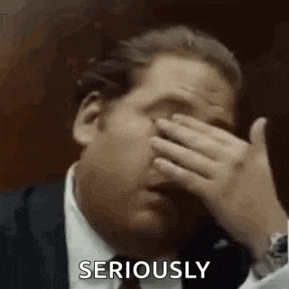 a man in a suit and tie is covering his face with his hand and saying `` seriously '' .