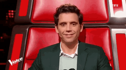a man in a green suit is sitting in a red chair with a microphone .
