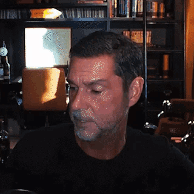 a man in a black shirt is sitting in front of a book shelf