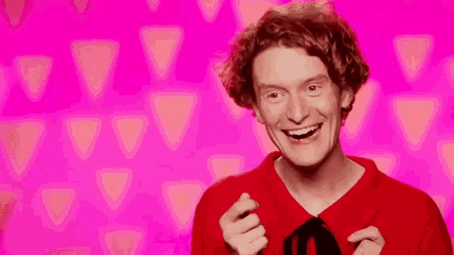 a young man with curly hair is wearing a red shirt and tie and smiling .
