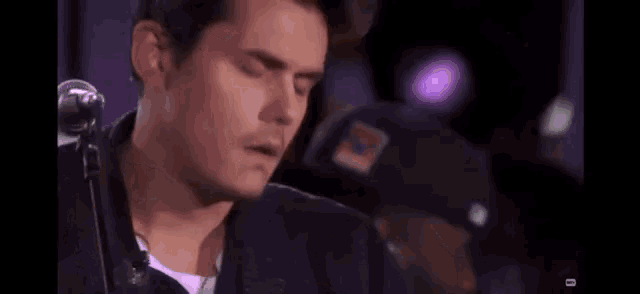 a close up of a man 's face with his eyes closed and a purple light behind him .
