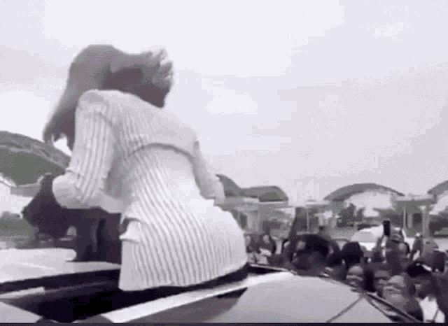a woman is sitting on the back of a car in front of a crowd of people taking pictures .