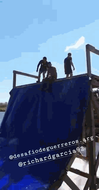 a group of people are standing on top of a large blue tarp .