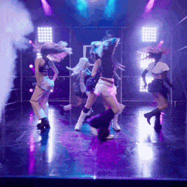 a group of women are dancing on a stage with purple lights and smoke