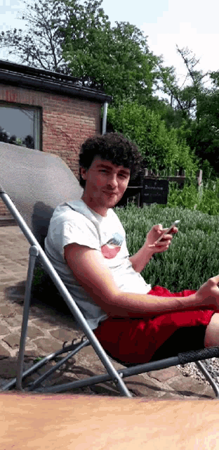 a young man is sitting in a chair looking at his phone