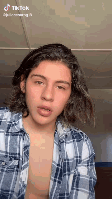 a young man with long hair is wearing a plaid shirt without a shirt on
