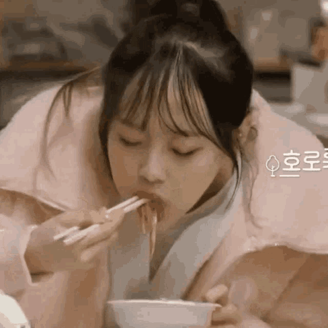 a woman in a pink jacket is eating noodles with chopsticks from a bowl .