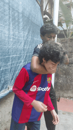 a boy wearing a spotify shirt is carrying another boy