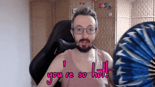 a man with glasses and a beard is holding a fan and says " you re so hot "