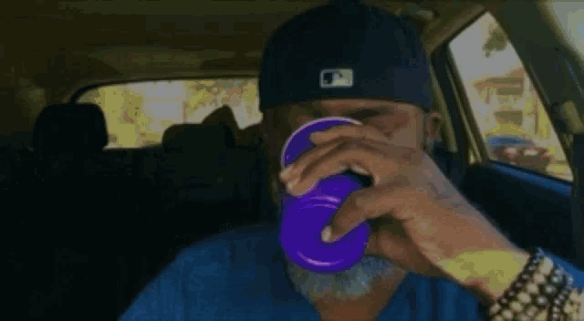 a man wearing a blue hat and a blue shirt is drinking from a purple cup
