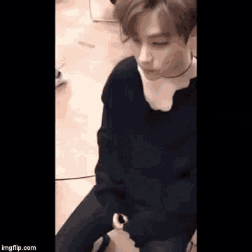 a man is sitting on the floor wearing a black sweater and a choker .