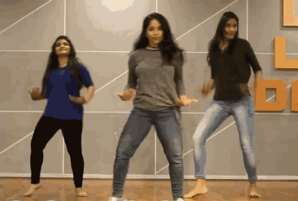 three women are dancing in a dance studio in front of a wall with the letter l on it