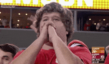 a man covering his mouth with his hands while watching a game between alabama and clemson