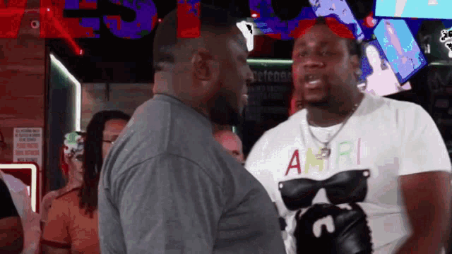 a man wearing a shirt with the letter a on it is talking to another man