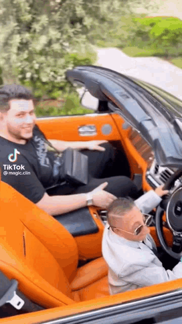 a man is driving a convertible car with a child in the back seat .