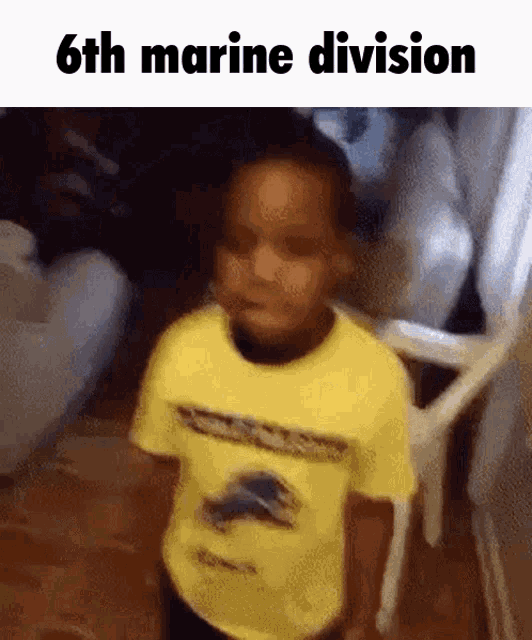 a young boy in a yellow shirt is standing in front of a chair with the words 6th marine division below him .