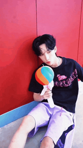 a young man is sitting on the ground holding a colorful lollipop .