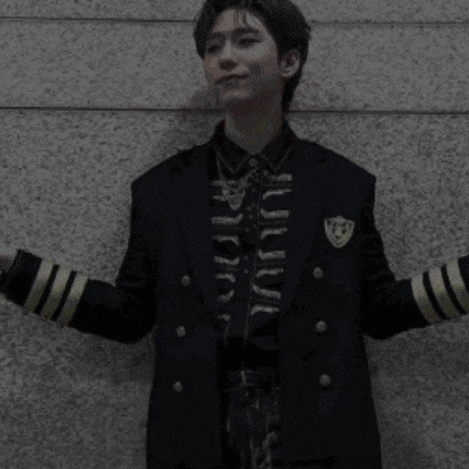 a young man wearing a black jacket and gold sleeves is standing in front of a wall .