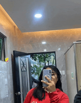 a woman in a red sweatshirt is taking a selfie in a mirror .