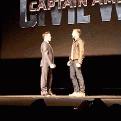 two men standing on a stage in front of a sign that says captain america civil war .