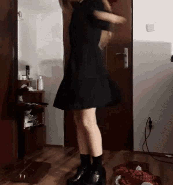 a woman in a black dress and black boots is dancing in a room