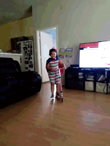 a little girl in a striped dress is riding a scooter in a living room