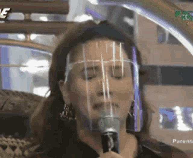 a woman wearing a face shield is speaking into a microphone .