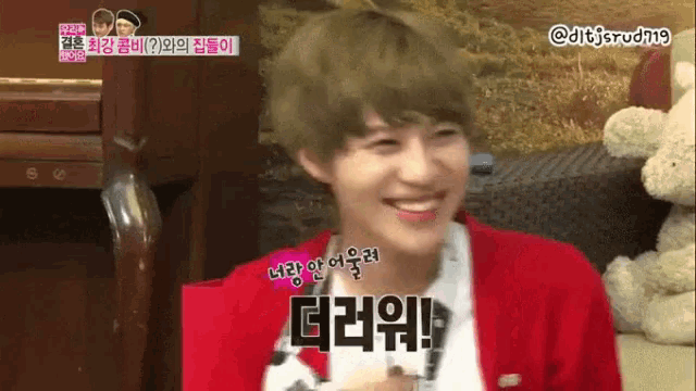 a man in a red jacket is smiling with a teddy bear behind him