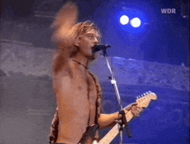 a shirtless man is singing into a microphone while playing a guitar