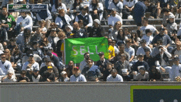 a crowd of people at a yankees baseball game holding a green sign that says sell