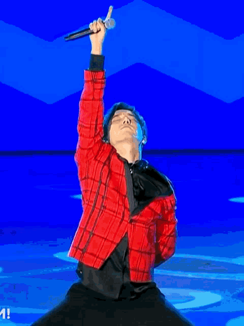 a man in a red plaid shirt and black jacket is standing in front of a blue wall .
