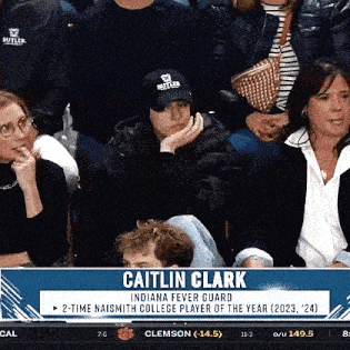 a group of people are sitting in a stadium watching a game and one of them is wearing a hat .